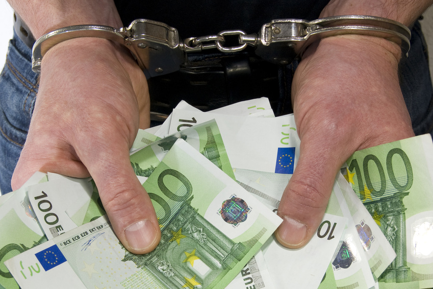 Mit Handschellen gefesselte Hände halten viele Geldscheine.